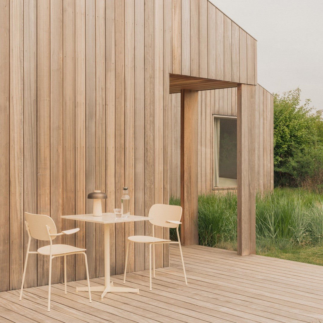 "Minimalist beige chairs and table on wooden deck with natural greenery backdrop."