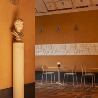 Warm amber wall with classical motifs, beige decorative band, and intricate patterned floor tiles. Modern clear chairs.