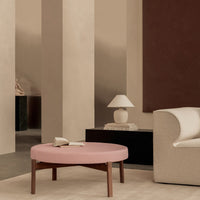 Round pink coffee table with wooden legs in a minimalist beige and brown interior setting. Modern and stylish decor.