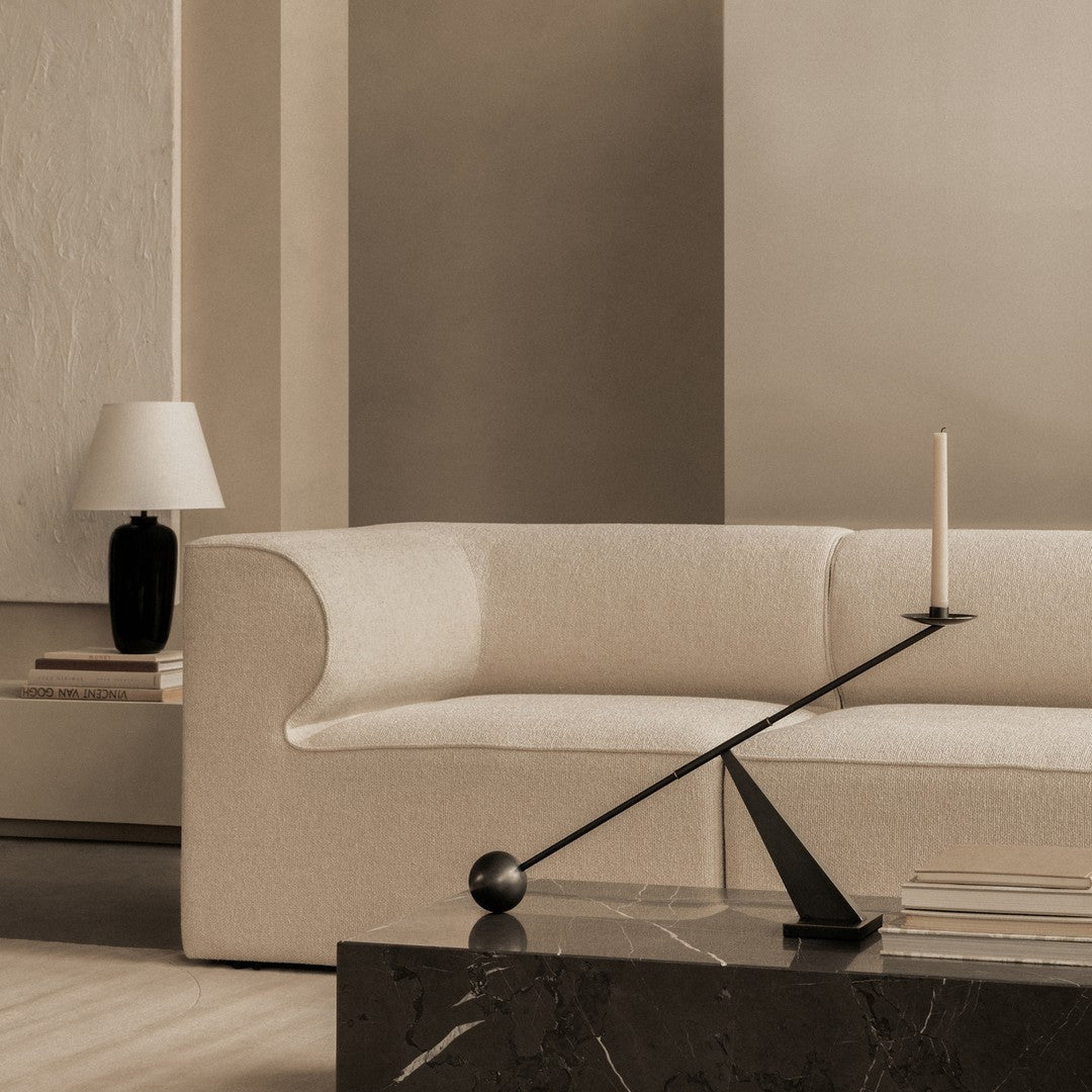 Neutral beige sofa with soft texture, accompanied by a sleek black candle holder and geometric shapes on a dark marble table.