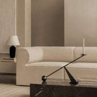 Neutral beige sofa with soft texture, accompanied by a sleek black candle holder and geometric shapes on a dark marble table.