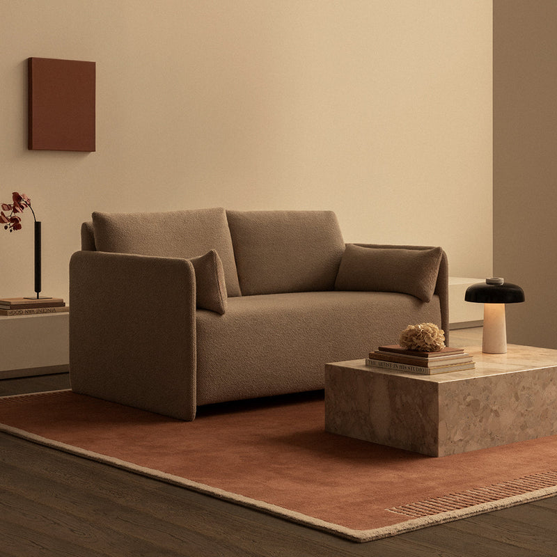 Brown fabric sofa with matching rug and earthy tones, complemented by a beige wall and subtle patterns for a cozy aesthetic.