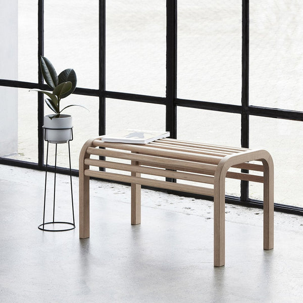 Light wood bench with curved slats, set against a black and white backdrop, featuring a minimalist design.