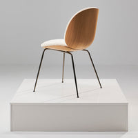 Modern wooden chair with a light beige seat and sleek black metal legs, displayed on a minimalistic white platform.