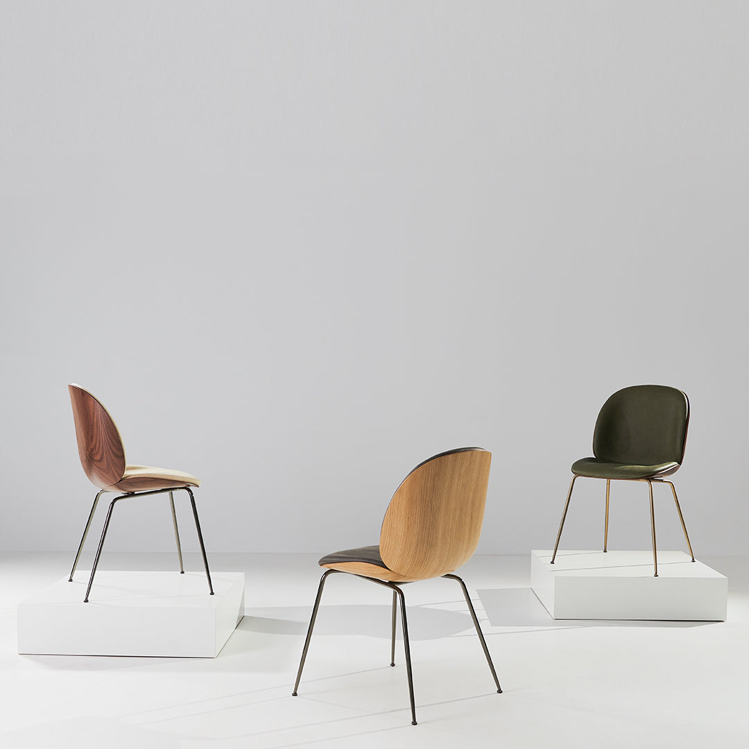 "Three modern chairs in brown, green, and light wood tones on white pedestals against a simple gray background."