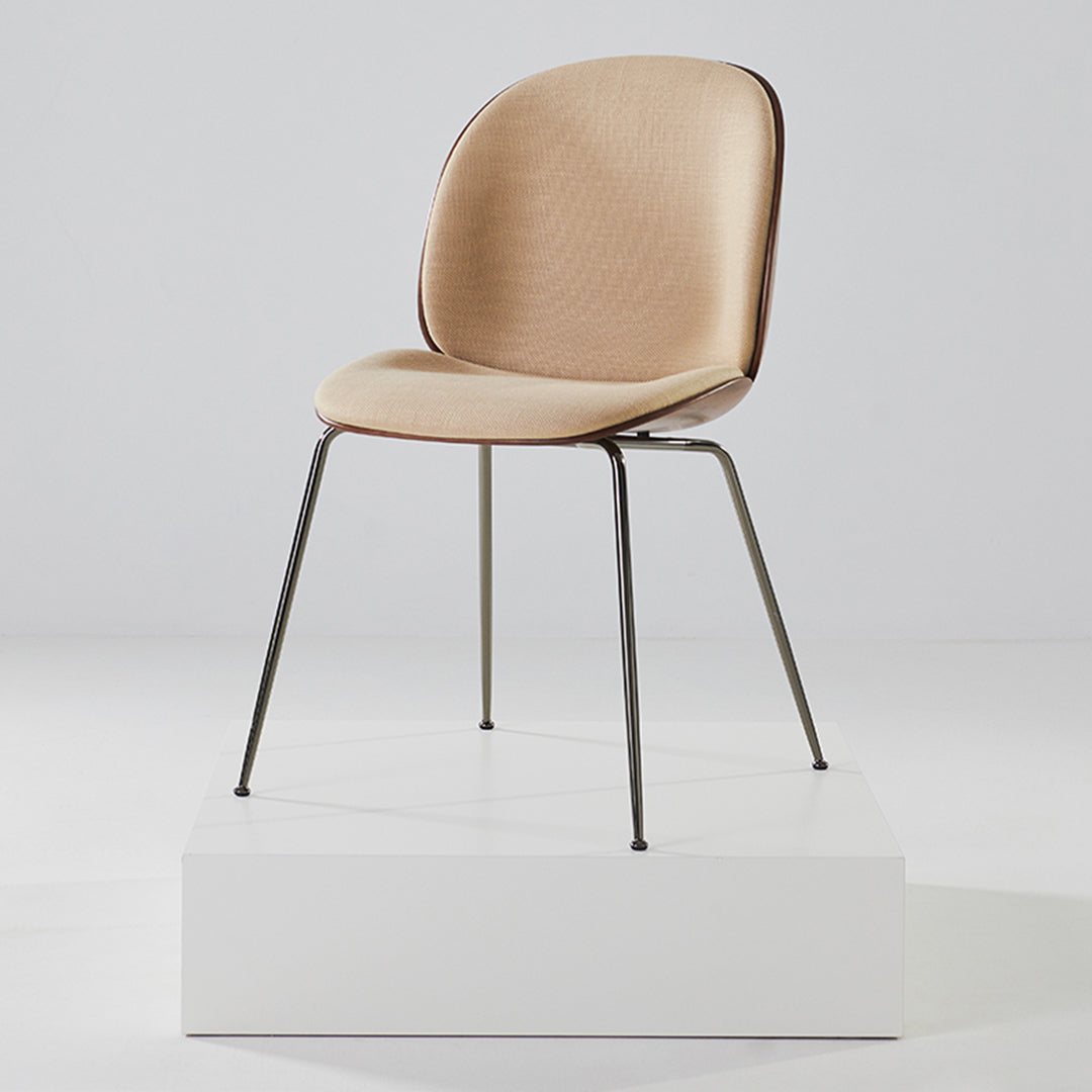 Beige upholstered chair with a smooth texture and sleek black metal legs, set on a white pedestal.