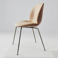 Tan upholstered chair with a sleek, minimalist design and slim metal legs on a white pedestal.