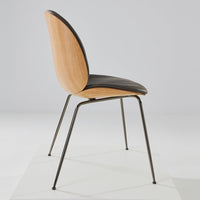 Side view of a modern chair featuring a light wood backrest, black seat, and sleek metal legs.