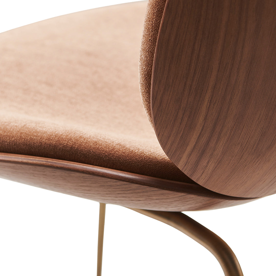 Close-up of a soft, blush velvet chair with a sleek wooden back and goldtone metal legs.