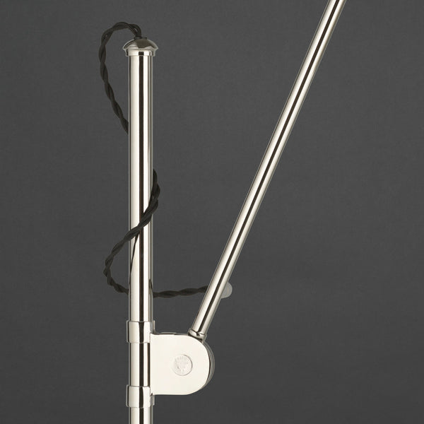 Polished silver metal lamp stand with a twisted black cord against a dark gray background.