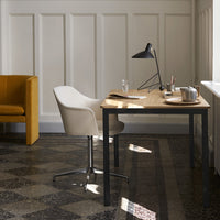 Modern workspace featuring a light wood desk, white chair, yellow accent chair, and patterned dark floor tiles.