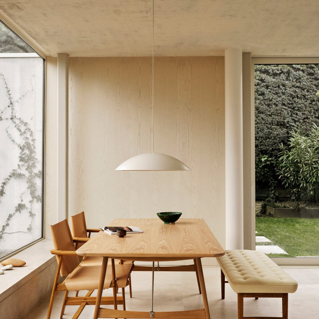 Contemporary wooden dining table with tan leather chairs, beige walls, and a minimalist white pendant light.