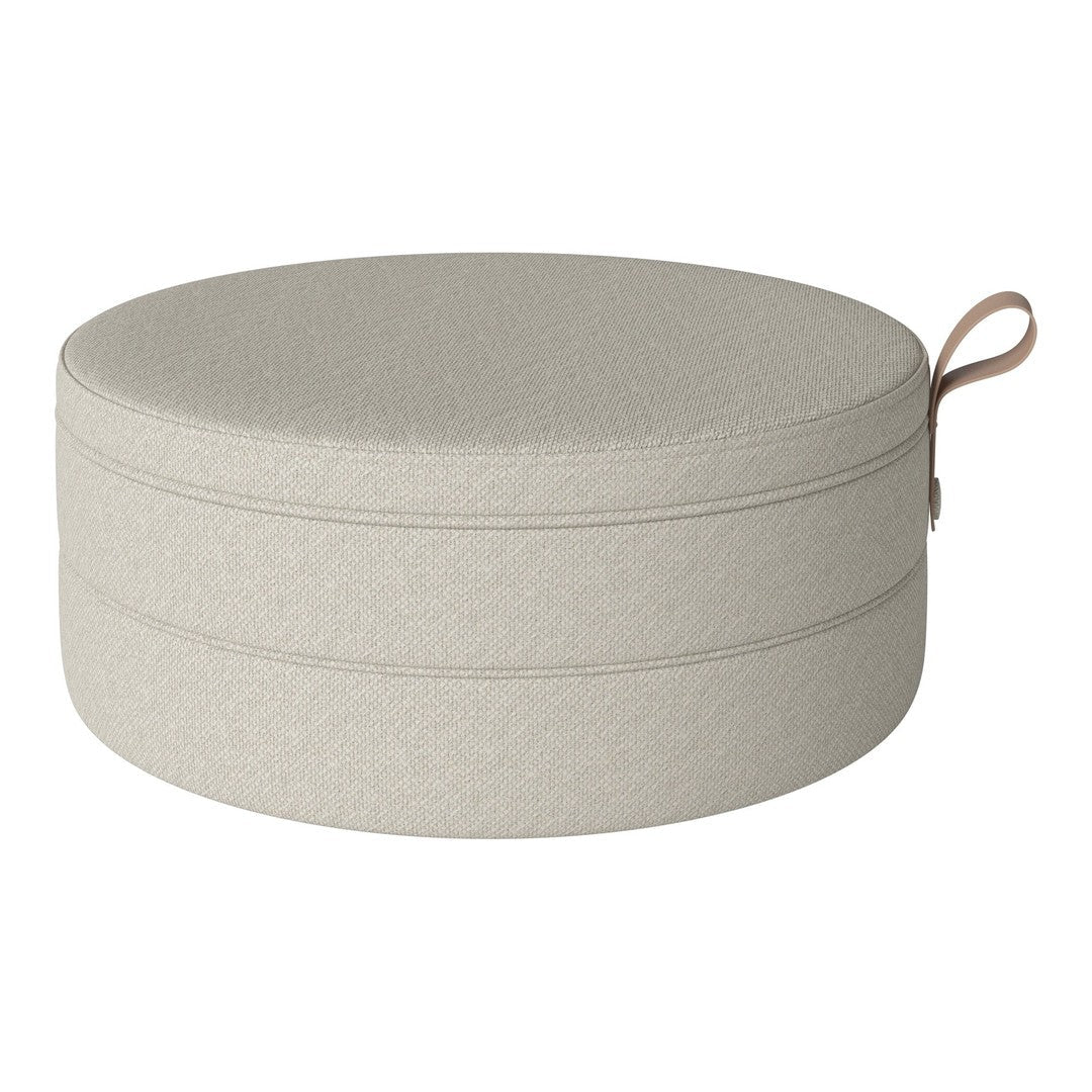Round storage ottoman in soft beige fabric with subtle texture and a stylish handle for easy mobility.