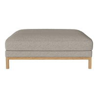 Light gray upholstered ottoman with a minimalist design and natural wood base. Soft, textured fabric complements neutral decor.