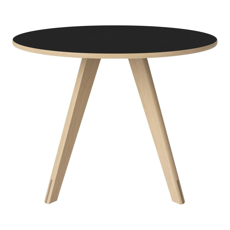 Round black table with natural wood legs, showcasing a minimalist design and contrasting colors. Perfect for modern decor.