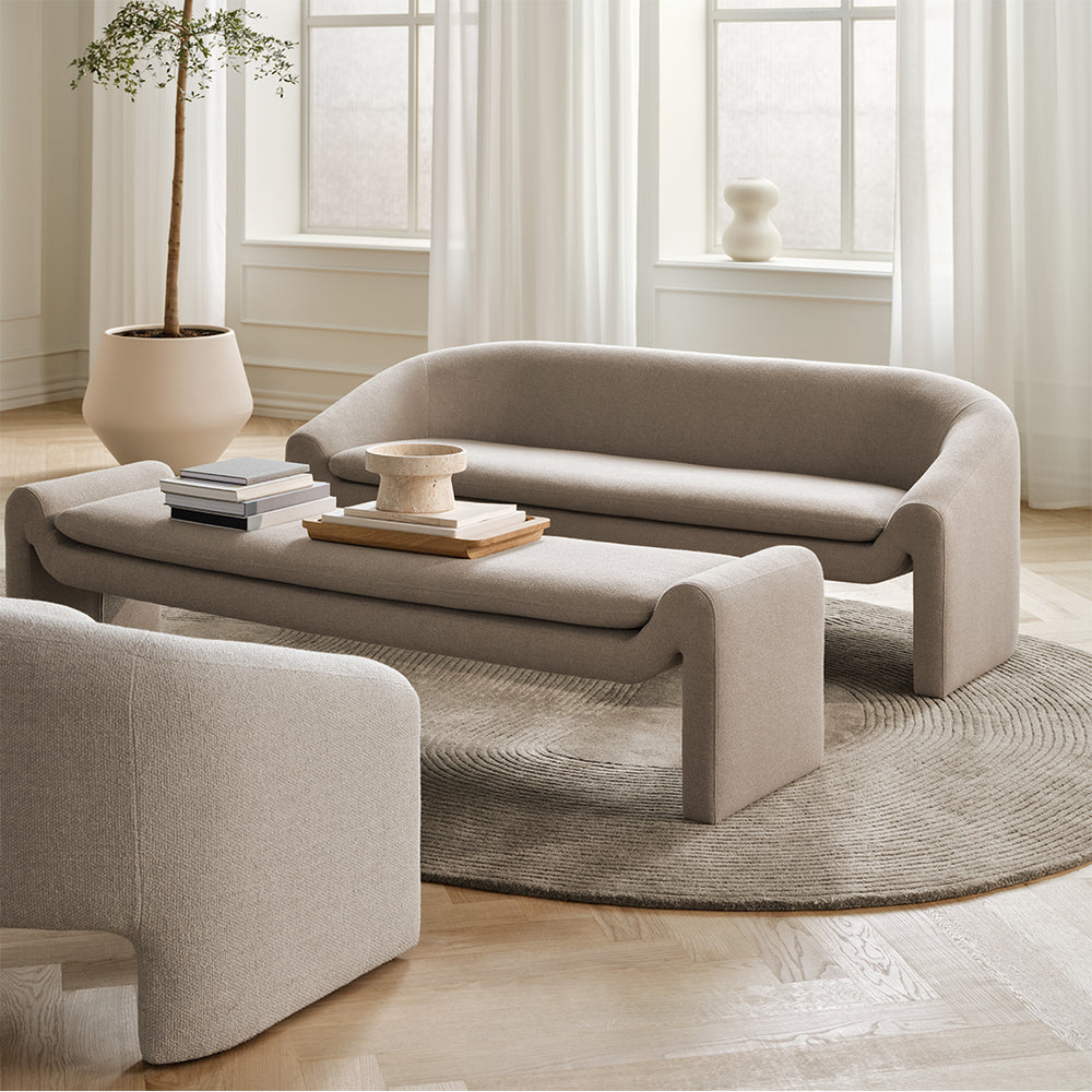 Modern living room with beige sofa and long ottoman coffee table by BOLIA in a bright room.