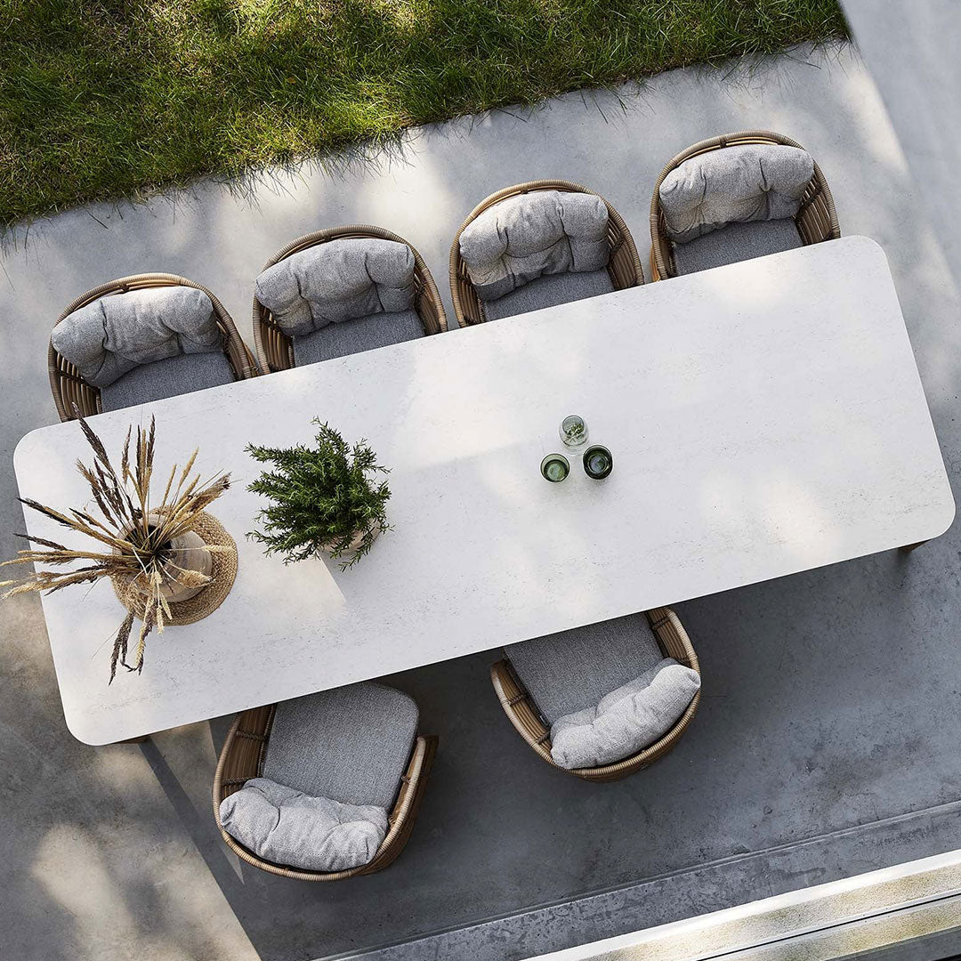 Stylish outdoor dining set with a white tabletop, gray cushioned chairs, and natural wicker accents. Perfect for any patio.