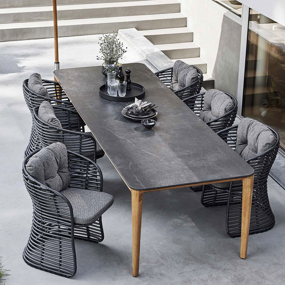 "Modern outdoor dining set featuring a sleek black tabletop, gray upholstered chairs, and warm wooden accents."