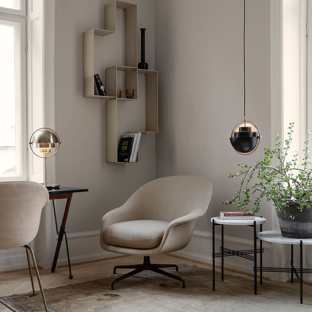 Beige accent chair with soft texture, black and gold pendant lights, and geometric décor against a neutral-toned wall.