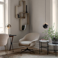 Beige accent chair with soft texture, black and gold pendant lights, and geometric décor against a neutral-toned wall.