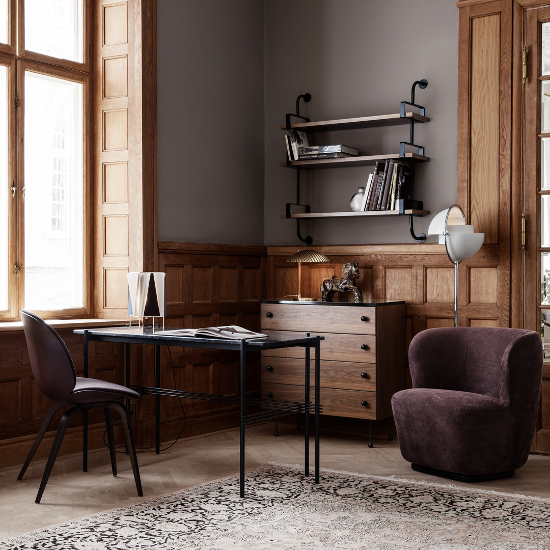 Modern office setup featuring a neutral gray wall, warm wood tones, and a plush dark purple chair against a patterned rug.