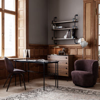 Modern office setup featuring a neutral gray wall, warm wood tones, and a plush dark purple chair against a patterned rug.