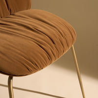 Brown velvet chair with soft, textured pleats and sleek gold legs against a neutral background.