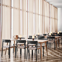 Elegant dining area with light beige curtains, wooden tables, black chairs, and a striped pattern on chair seats.