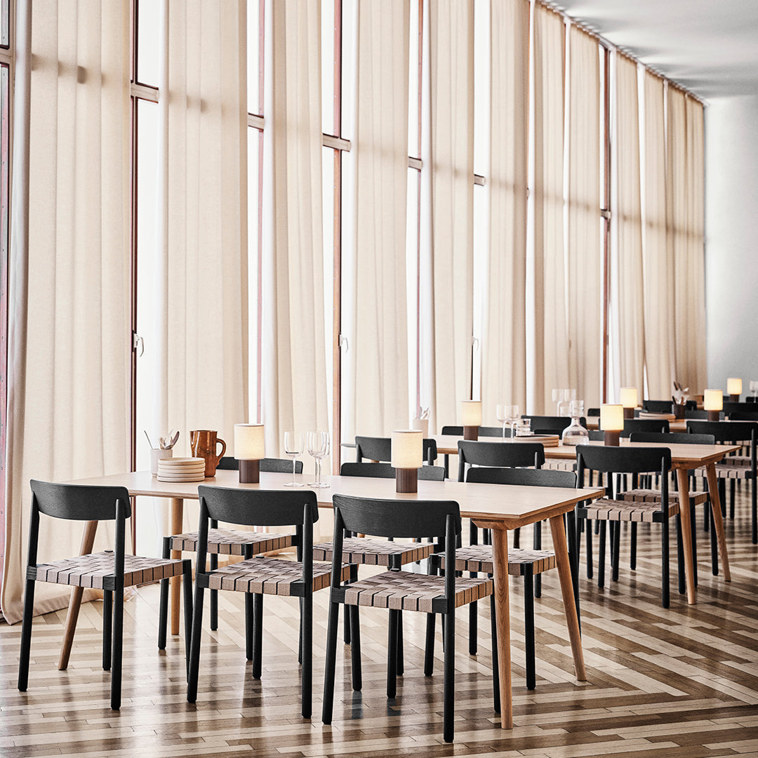 Elegant dining area with light beige curtains, wooden tables, black chairs, and a striped pattern on chair seats.