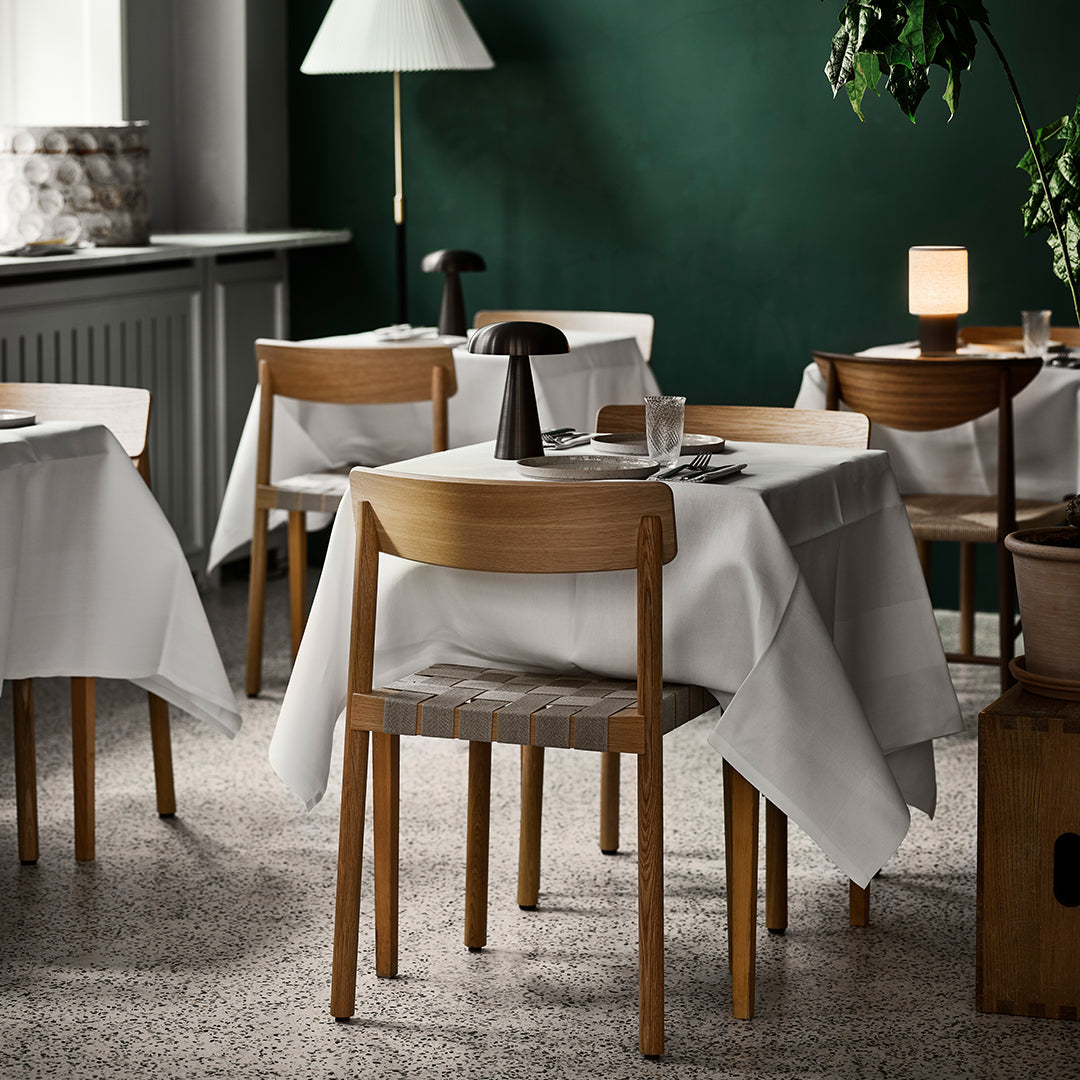 Elegant white tablecloths on wooden tables in a cozy green restaurant setting with soft lighting and neutral tones.