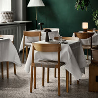 Elegant white tablecloths on wooden tables in a cozy green restaurant setting with soft lighting and neutral tones.