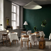 Elegant dining space featuring a dark green wall, white tablecloths, brown wooden chairs, and soft lighting.