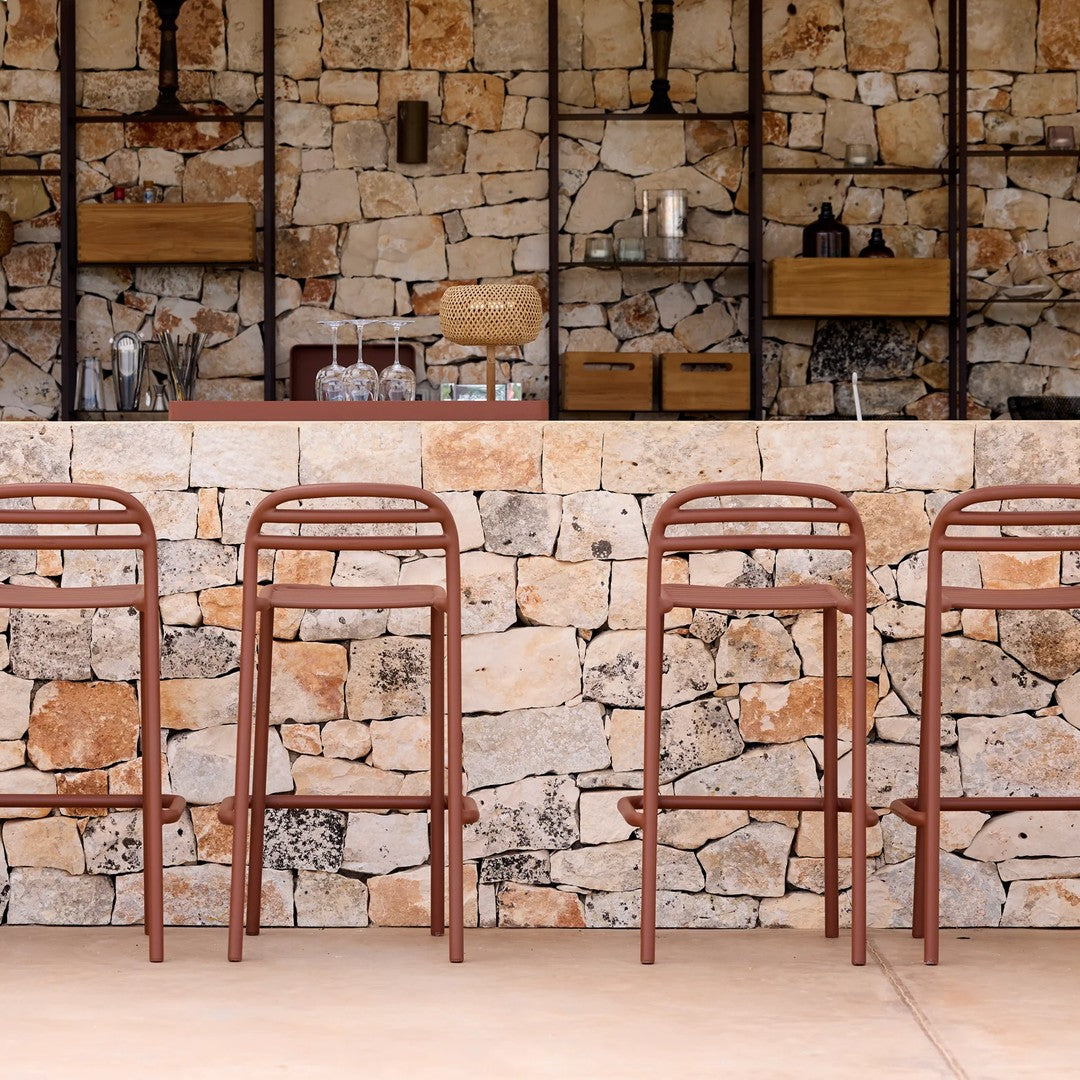 Rust-orange bar stools against a textured stone wall with varied natural hues, enhancing a rustic decor aesthetic.