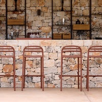 Rust-orange bar stools against a textured stone wall with varied natural hues, enhancing a rustic decor aesthetic.