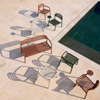 Colorful metal chairs and a table in red, green, white, and brown, casting intricate shadows on a light stone surface.