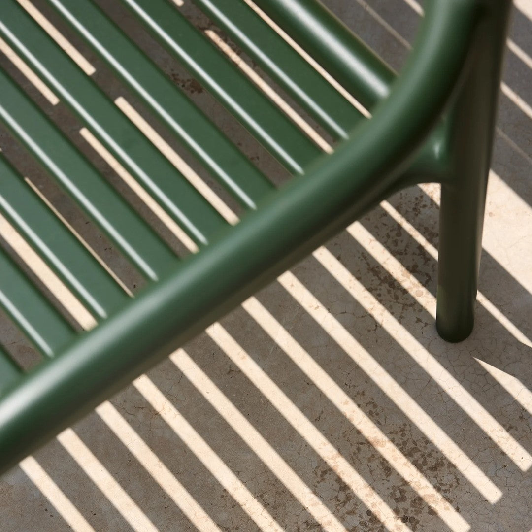 Green metal chair with slatted pattern casting striped shadows on a light gray surface.
