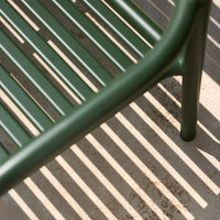 Green metal chair with slatted pattern casting striped shadows on a light gray surface.
