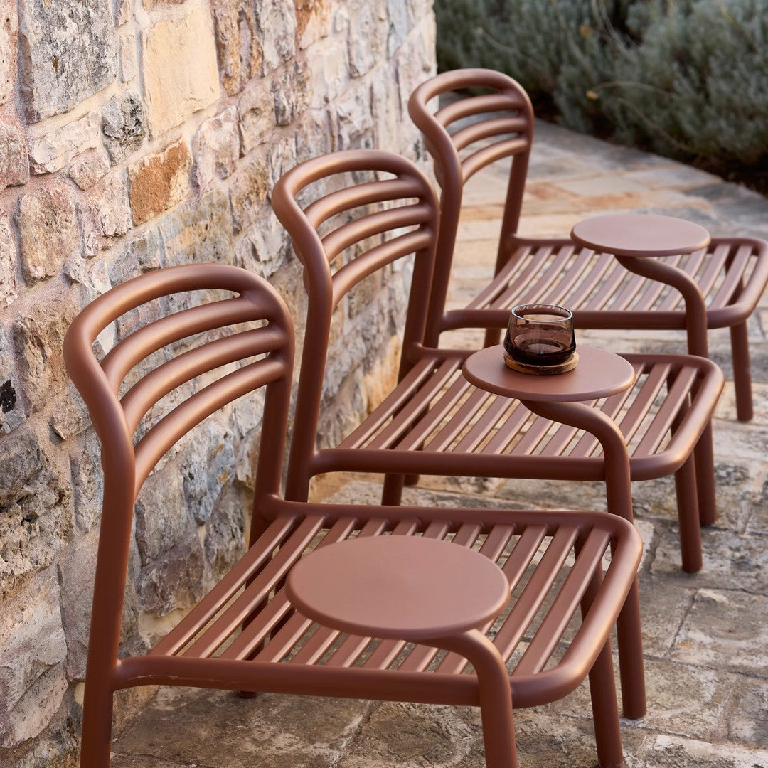 Three modern brown lounge chairs with striped seating, set against a textured stone wall in an outdoor setting.