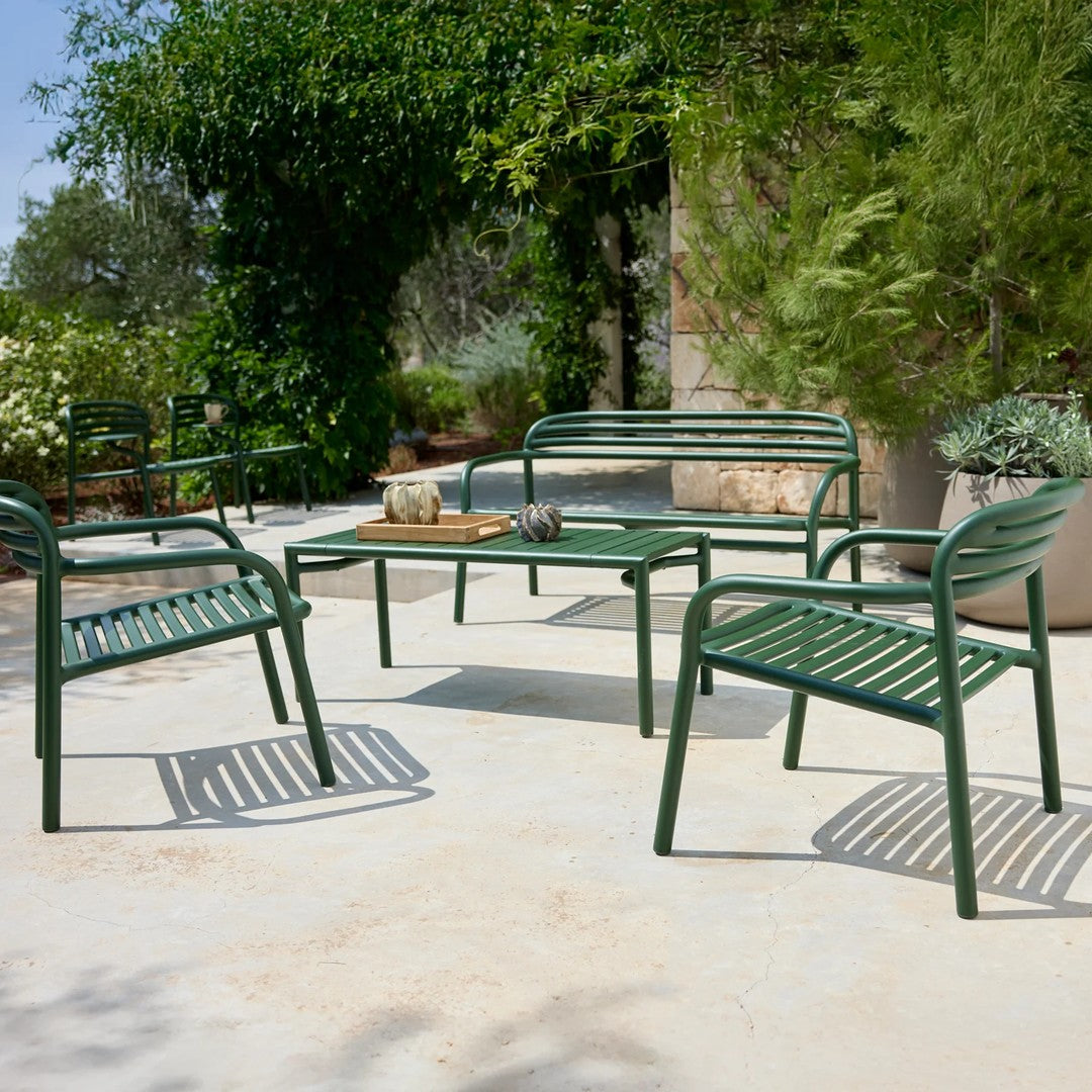Green metal patio furniture set with striped seating on a light concrete surface, surrounded by greenery.