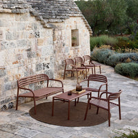 "Brown metal outdoor seating set with slatted design, featuring a circular brown rug against a stone background."