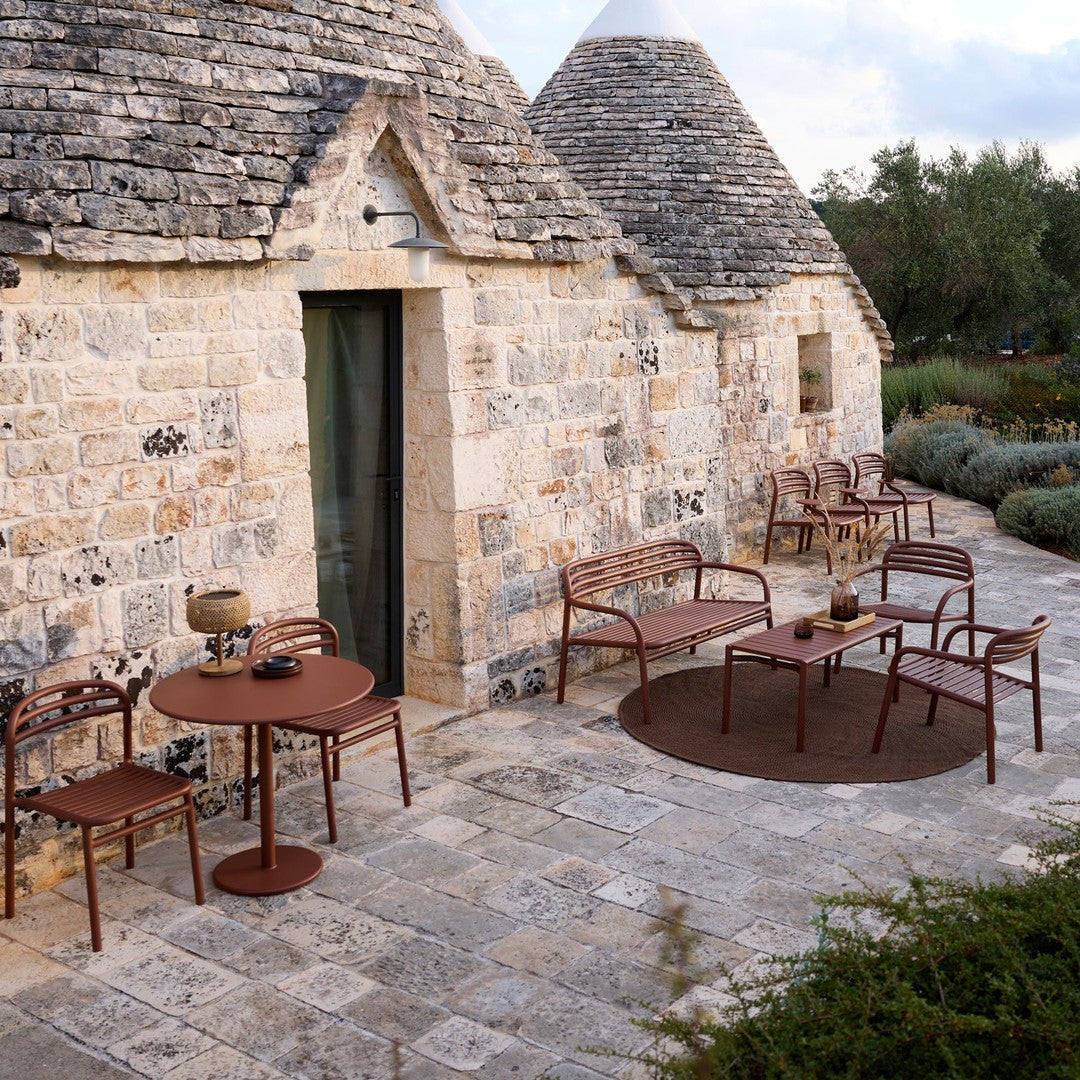 Rustic outdoor furniture set in warm brown tones, complemented by a circular patterned rug against a stone backdrop.