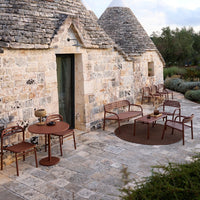 Rustic outdoor furniture set in warm brown tones, complemented by a circular patterned rug against a stone backdrop.