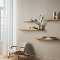 Light beige wall with wooden shelves displaying neutral decor; soft white curtains and a light gray chair enhance the calming palette.