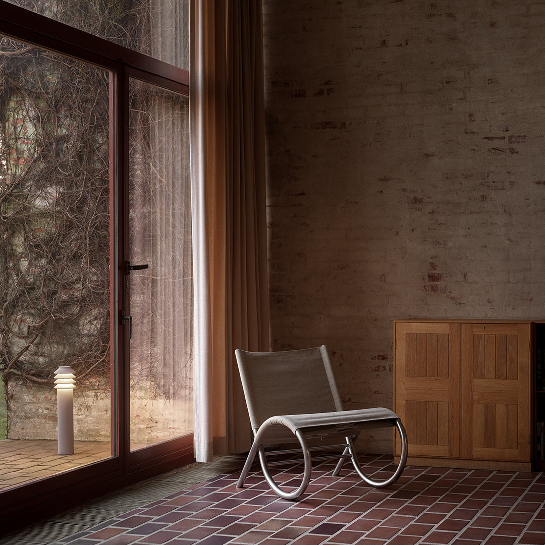 Minimalist chair with a soft gray mesh seat and curved white frame, set against warm wooden tones and earthy brick flooring.