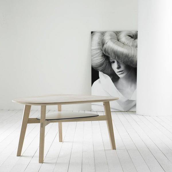 Light wood coffee table with smooth, minimalist design; complemented by a monochrome art piece in the background.