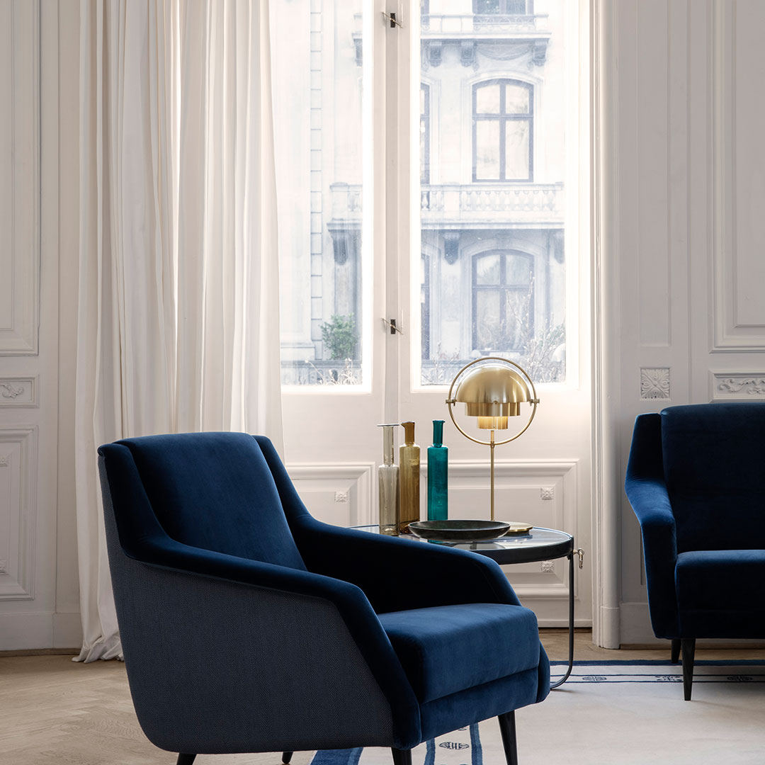 "Two elegant navy blue upholstered chairs with sleek lines, set against light curtains and a modern side table."