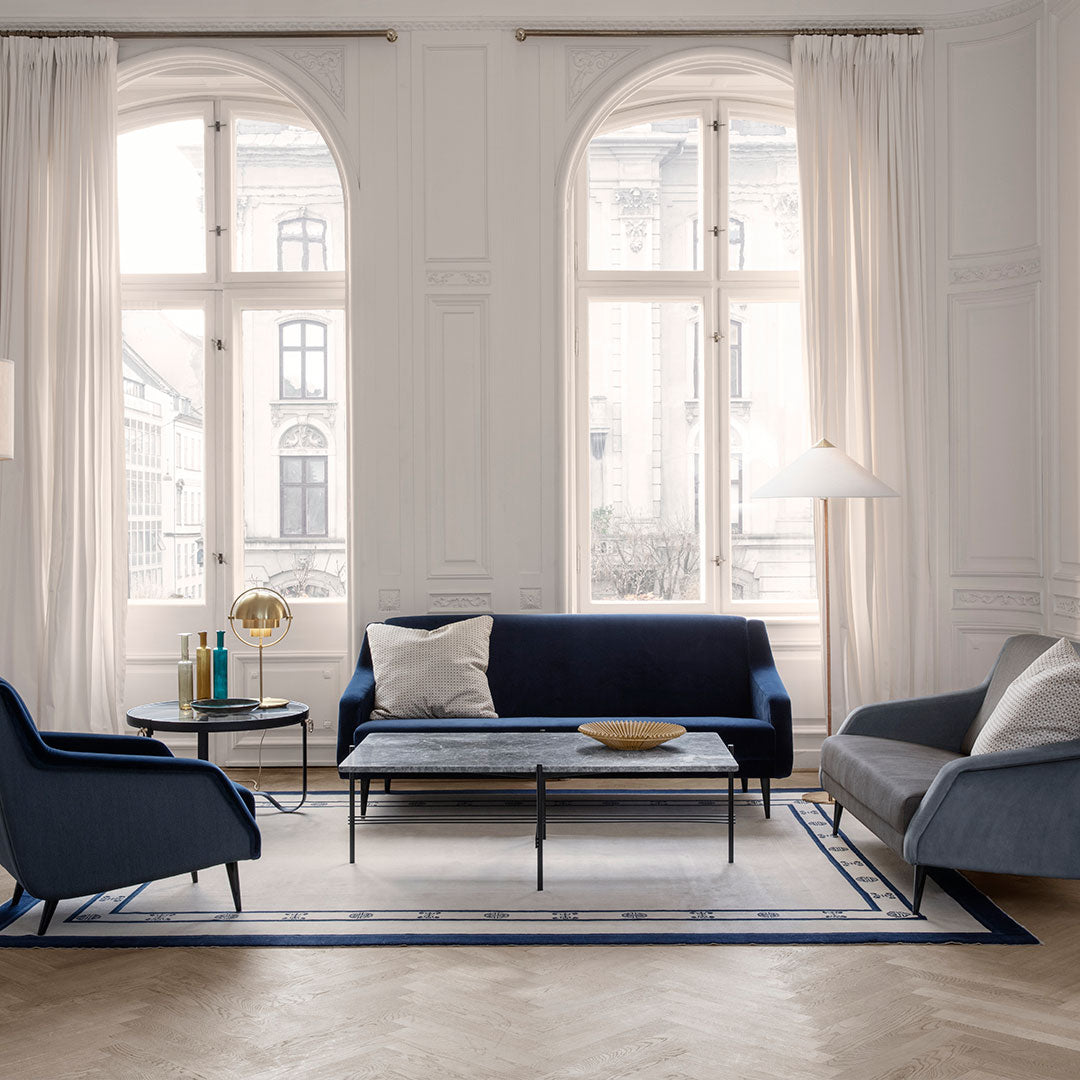Navy blue and light gray sofa set on a patterned rug with clean lines, surrounded by bright natural light.
