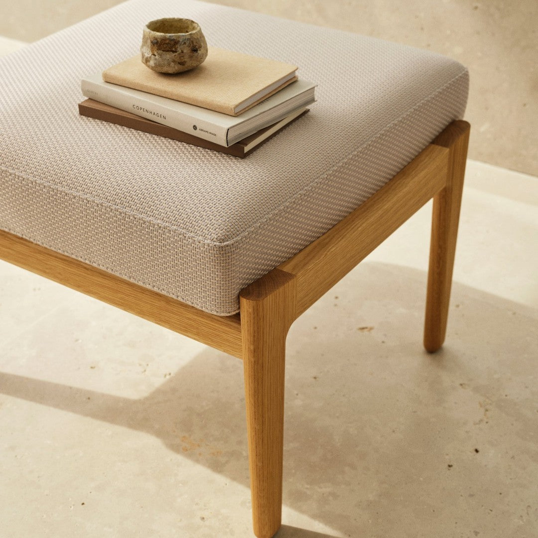 Beige textured cushion on a light wooden frame, complemented by stacked neutral-toned books and a ceramic cup.