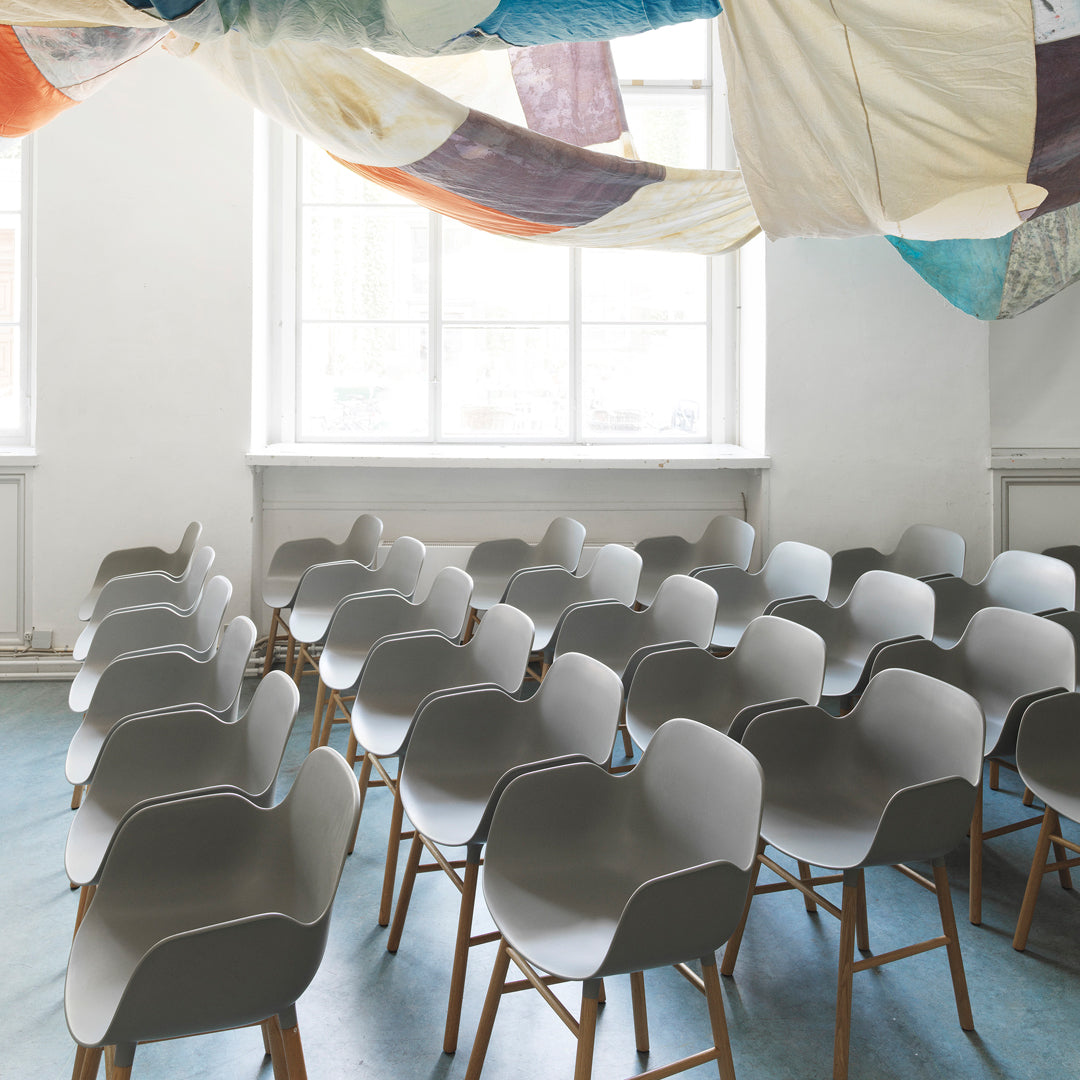 "Gray modern chairs with wooden legs in a bright, minimalist space featuring colorful patterned ceiling drapes."