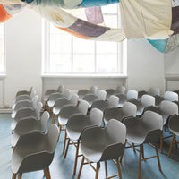 "Gray modern chairs with wooden legs in a bright, minimalist space featuring colorful patterned ceiling drapes."